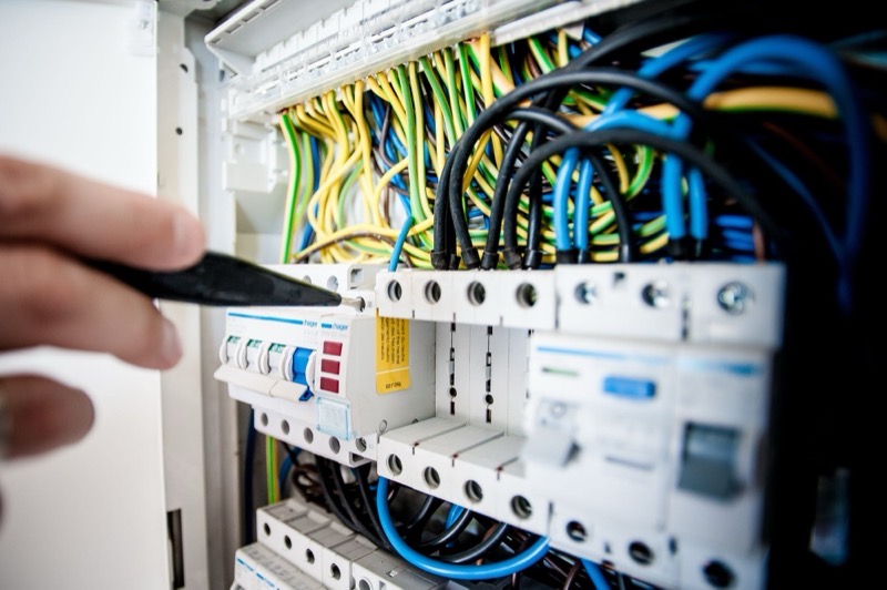Close-up of a consumer unit, a hand working among the circuit breakers and wiring